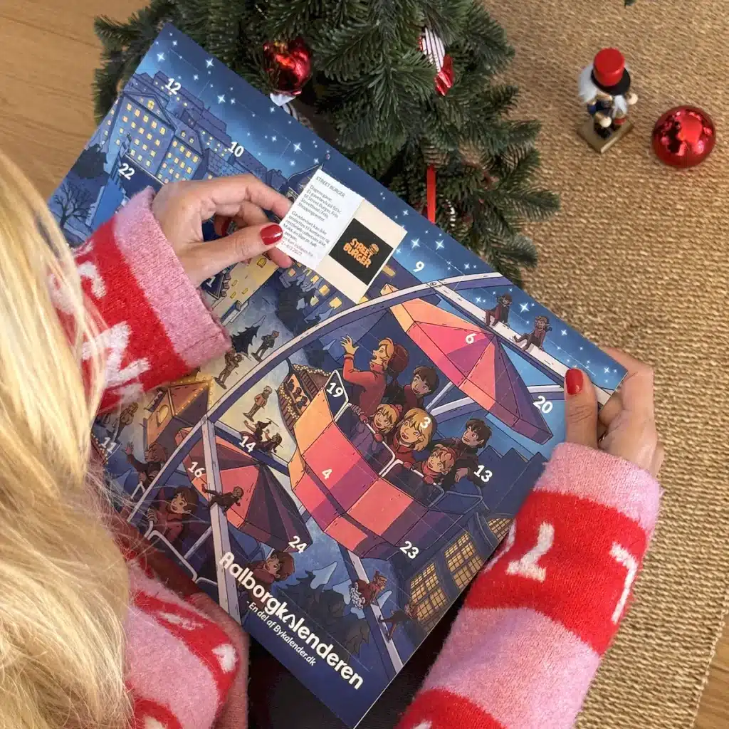 Kvinde i julesweater der åbner en låge i Aalborgkalenderen under juletræet