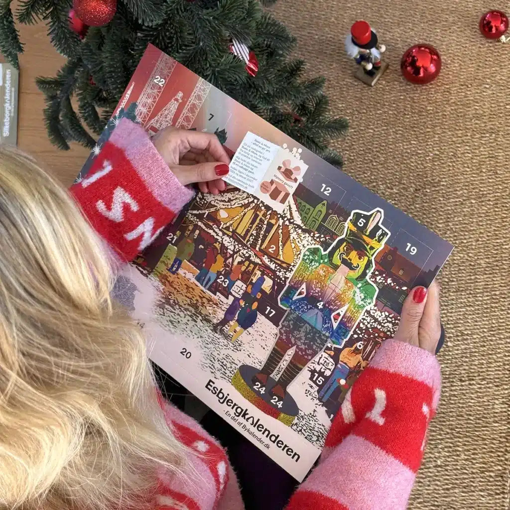 Kvinde i julesweater der åbner en låge i Esbjergkalenderen under juletræet