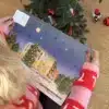 Kvinde i julesweater der åbner en låge i Hjørringkalenderen under juletræet