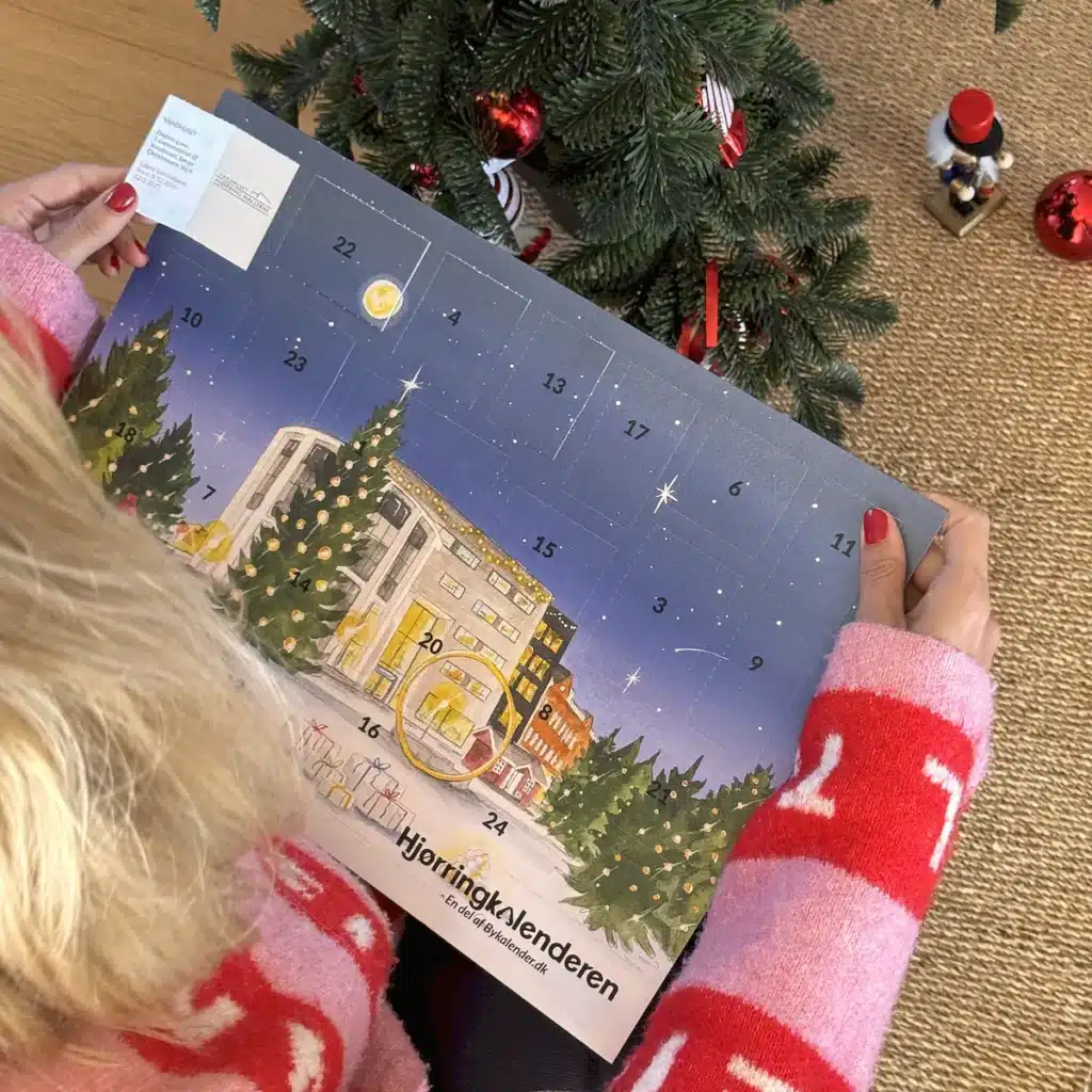 Kvinde i julesweater der åbner en låge i Hjørringkalenderen under juletræet