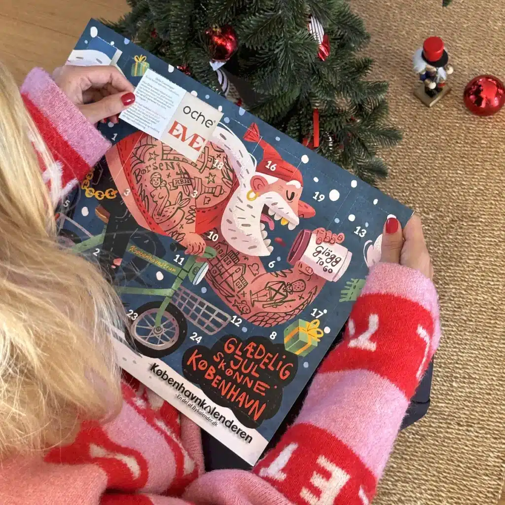 Kvinde i julesweater der åbner en låge i Københavnkalenderen under juletræet