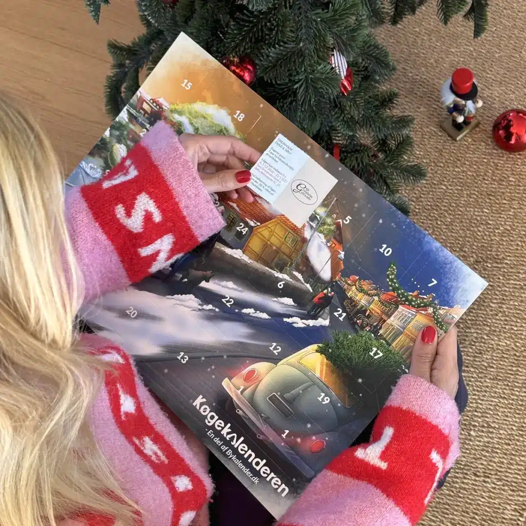 Kvinde i julesweater der åbner en låge i Køgekalenderen under juletræet