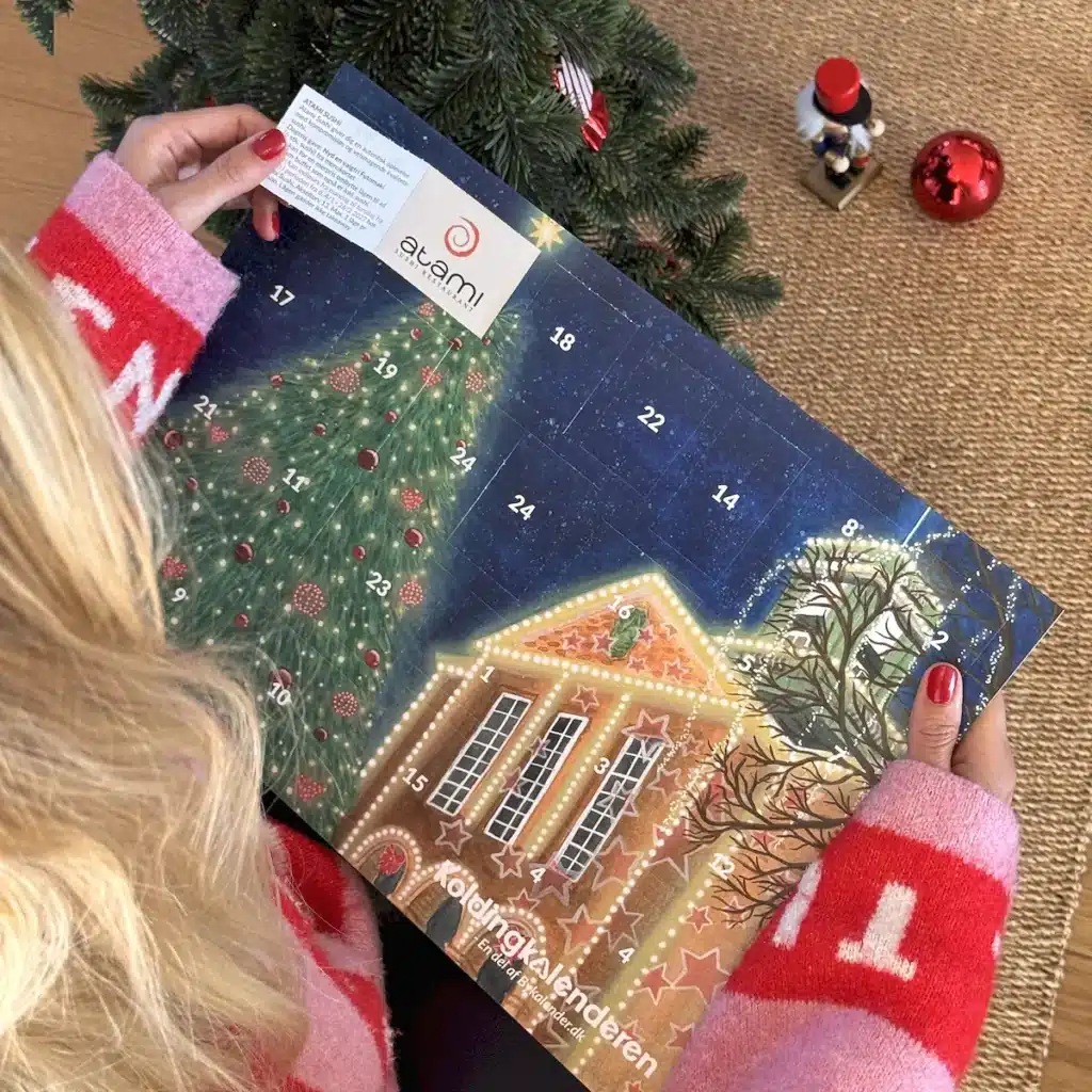 Kvinde i julesweater der åbner en låge i Koldingkalenderen under juletræet