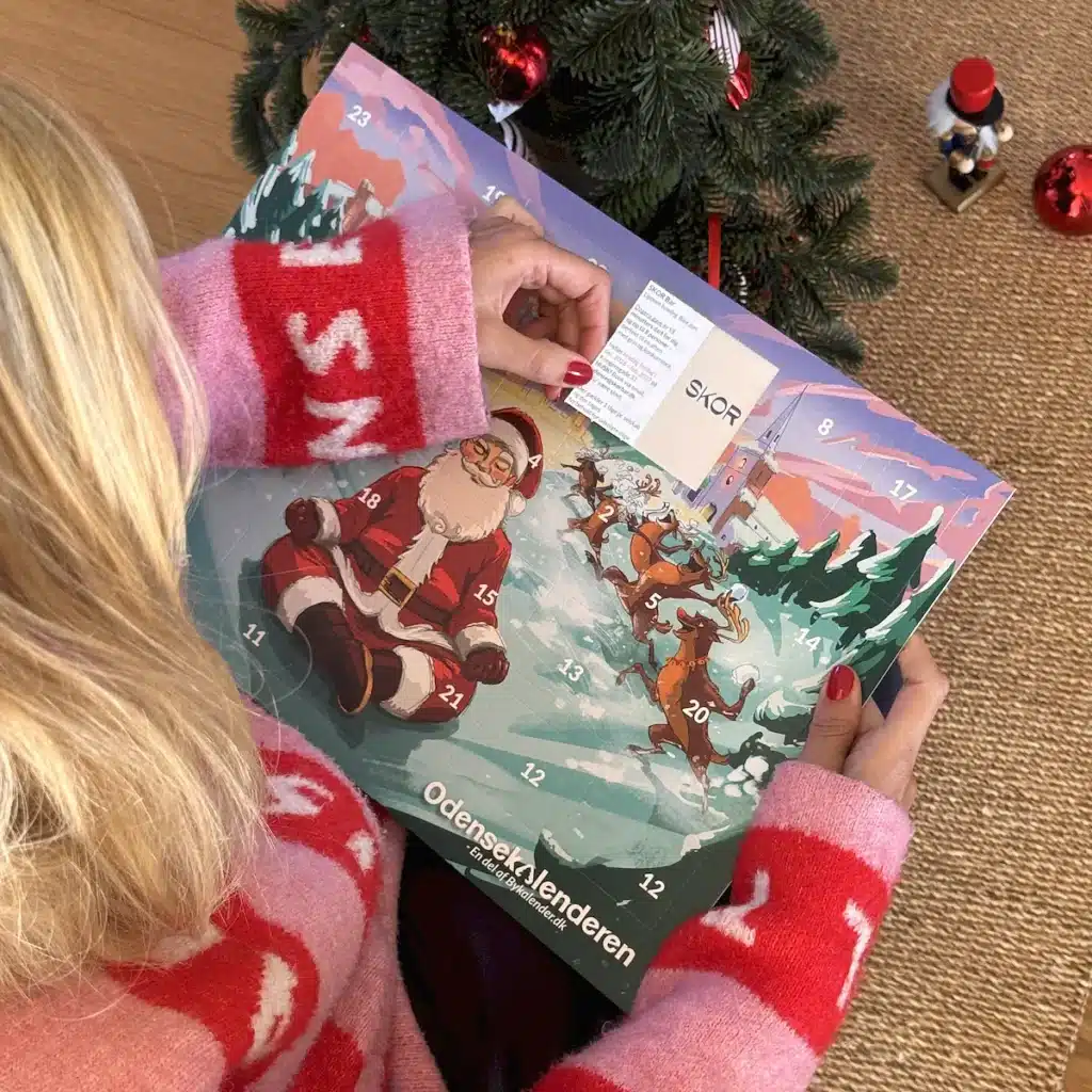 Kvinde i julesweater der åbner en låge i Odensekalenderen under juletræet