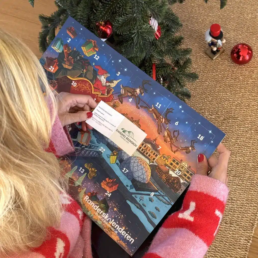 Kvinde i julesweater der åbner en låge i Randerskalenderen under juletræet
