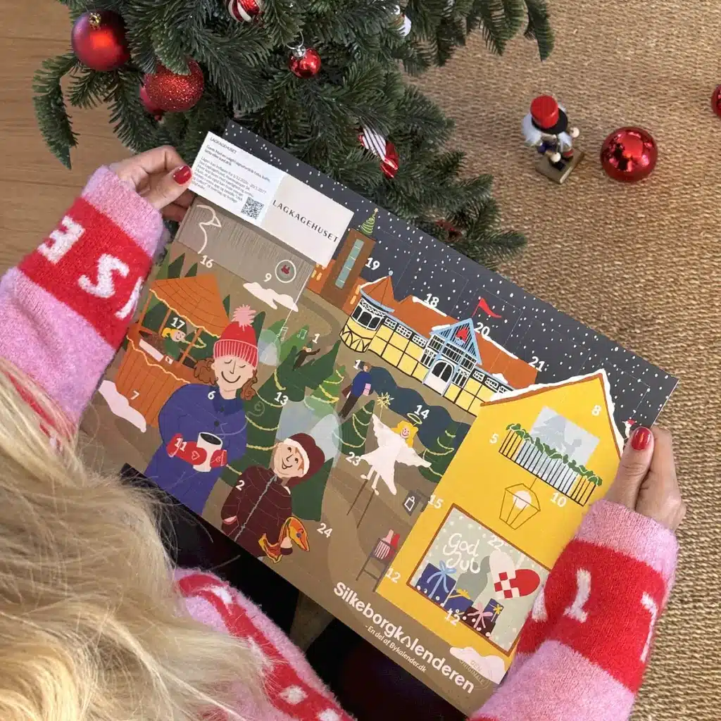 Kvinde i julesweater der åbner en låge i Silkeborgkalenderen under juletræet