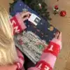 Kvinde i julesweater der åbner en låge i Vejlekalenderen under juletræet