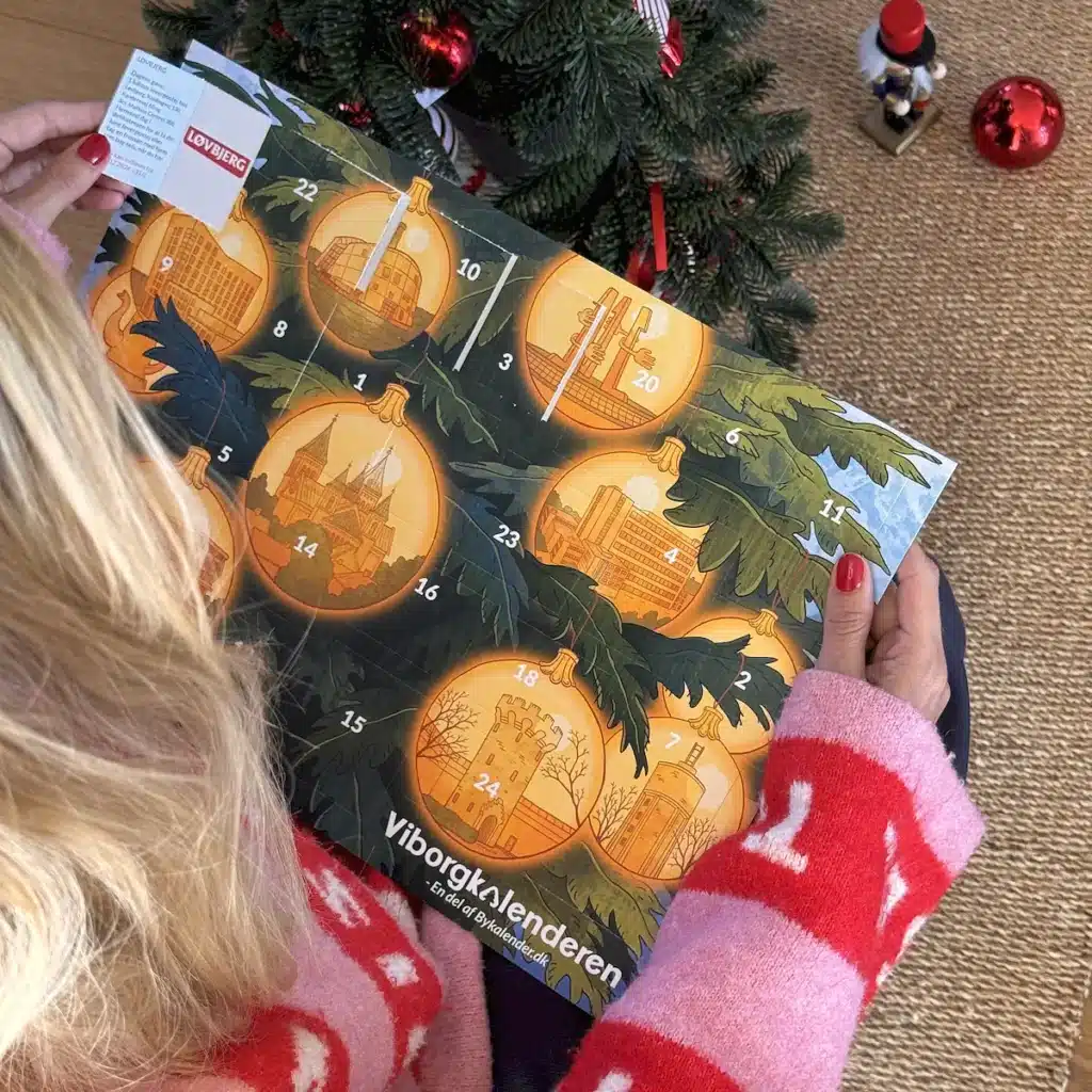Kvinde i julesweater der åbner en låge i Viborgkalenderen under juletræet